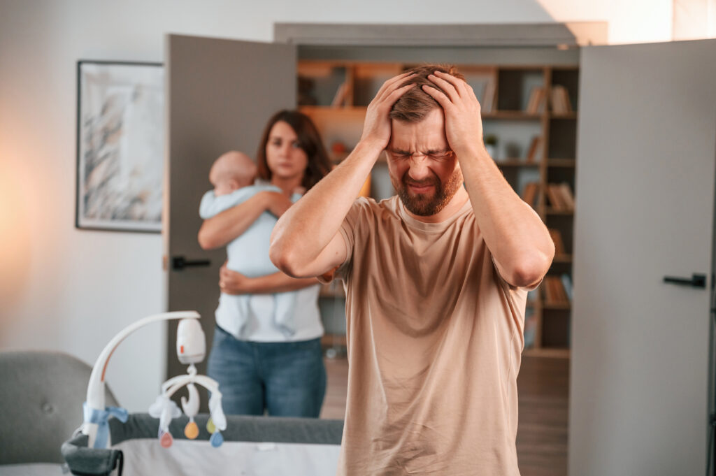 Having a headache. Conception of stress. Couple with newborn baby is at home having conflict.