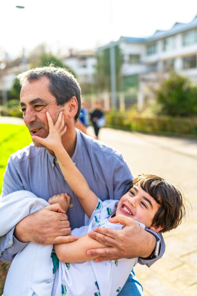 Grandfather having fun with his grandson, holding him and playing in a park, enjoying a sunny day