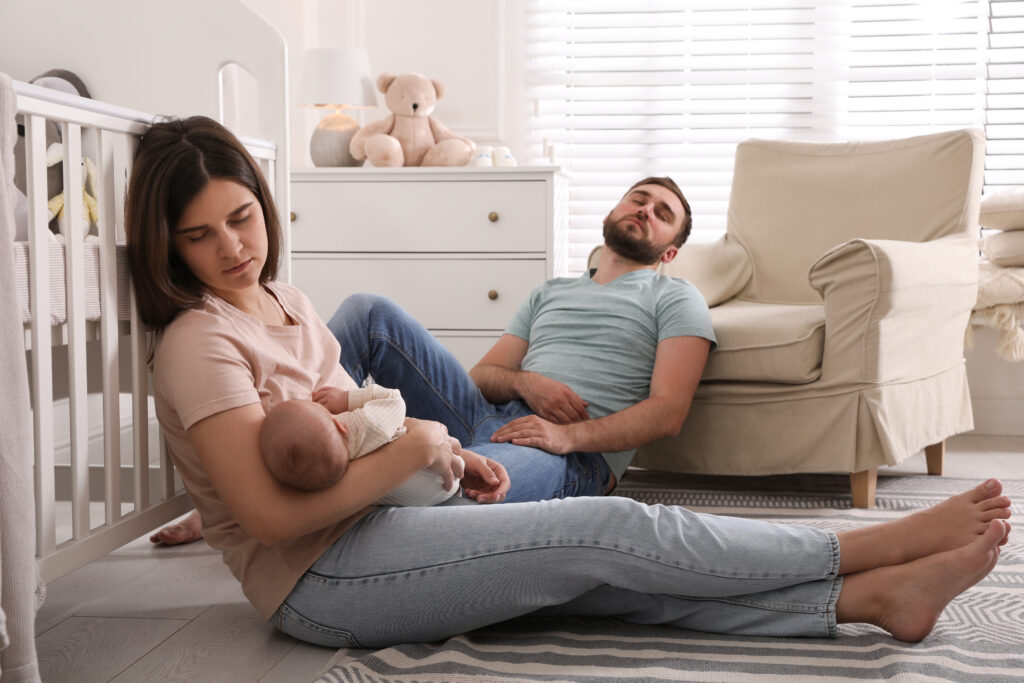 Tired young parents with their baby sleeping on floor in children's room
