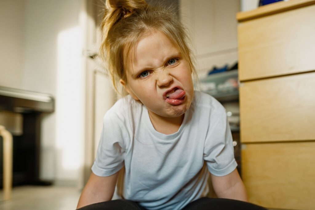 Funny, child girl with blue eyes at home on the floor plays and grimaces, makes faces into the camera. Headshot, close-up